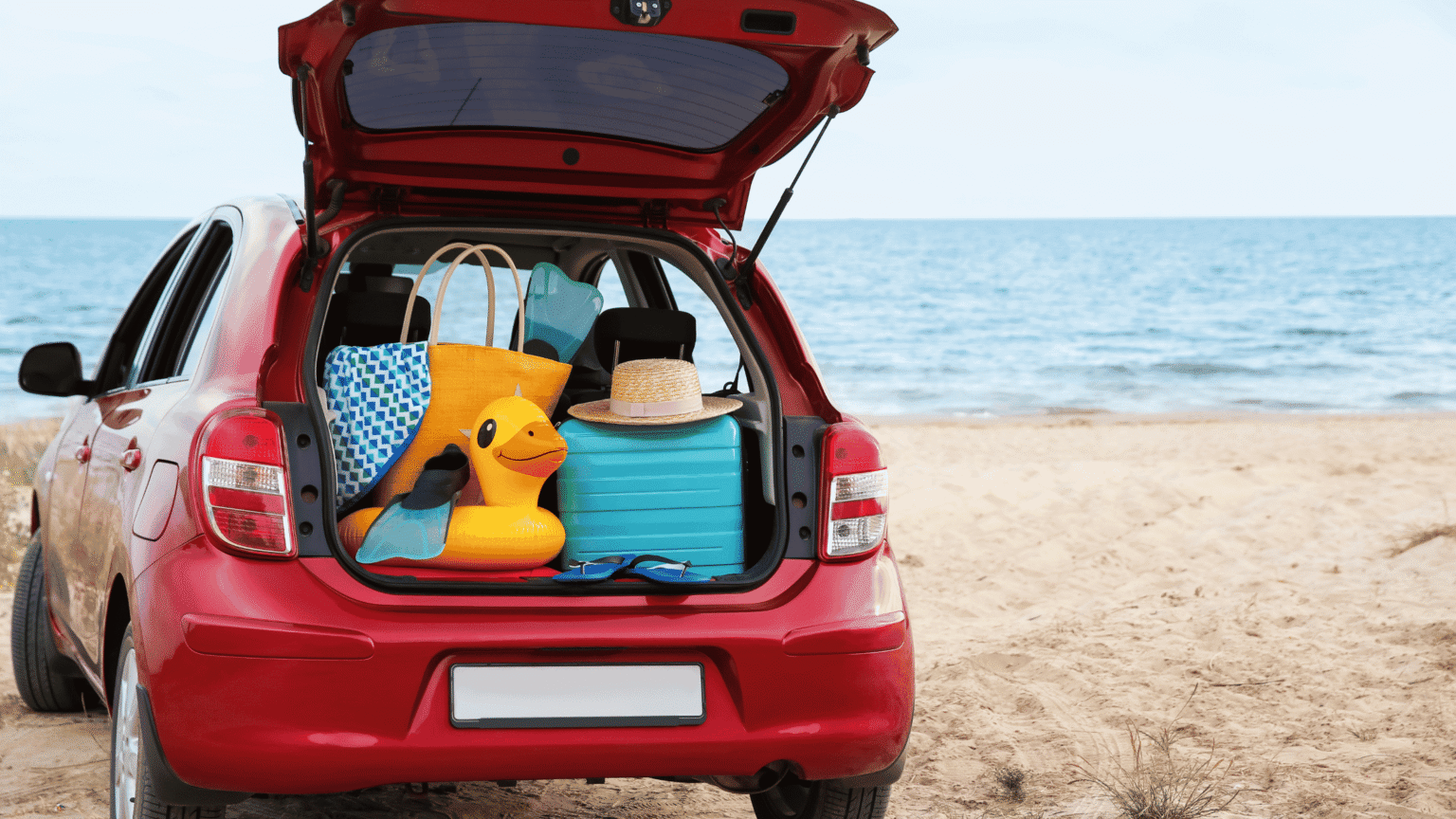 Car boot open on a beach packed with things.